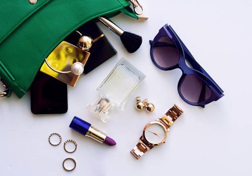 Top view of female fashion accessories for woman. Stylish sunglasses, green bag , gold watch , lipstick , perfume , rings , smartphone